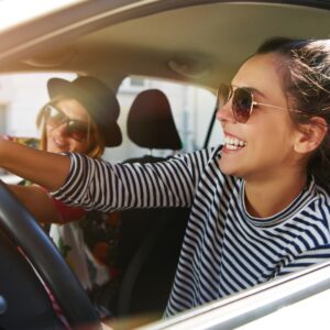 Mujer conduciendo sonriente su coche con una acompañante